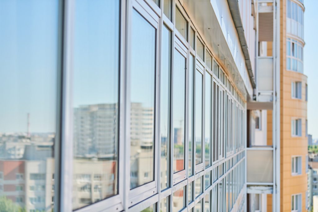 Facade of a modern high-rise with rows of blue glass windows reflecting the cityscape behind it, seen from an angled perspective.